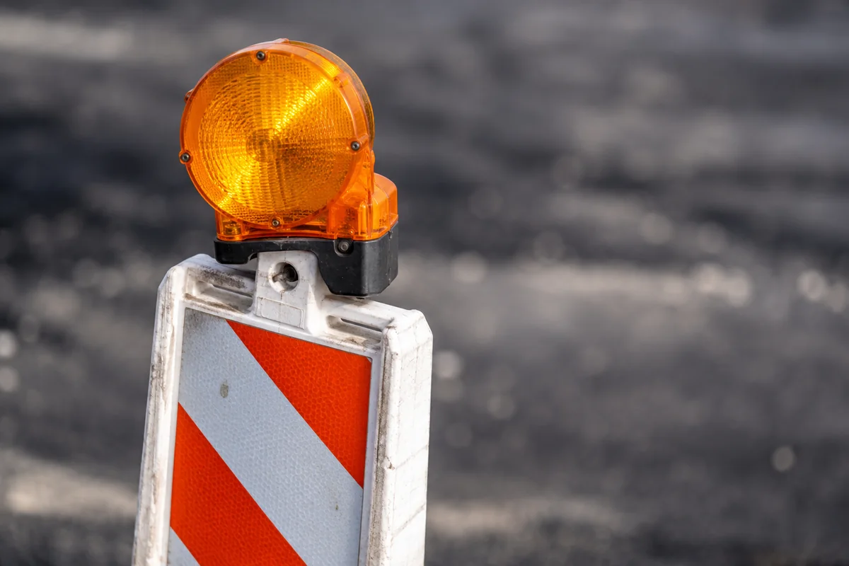 Orangeweiße Baustellenbake mit orangefarbener Warnleuchte auf Asphalt